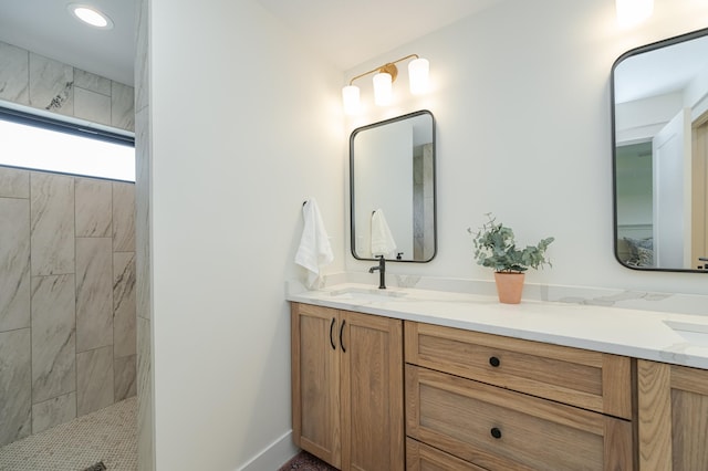 bathroom featuring a walk in shower, double vanity, a sink, and baseboards