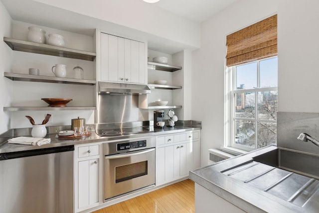 kitchen featuring light wood-type flooring, stainless steel appliances, white cabinets, and radiator heating unit