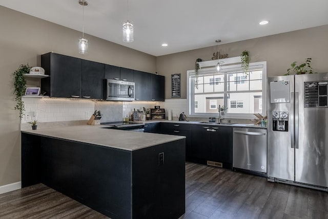 kitchen with stainless steel appliances, sink, kitchen peninsula, pendant lighting, and dark wood-type flooring