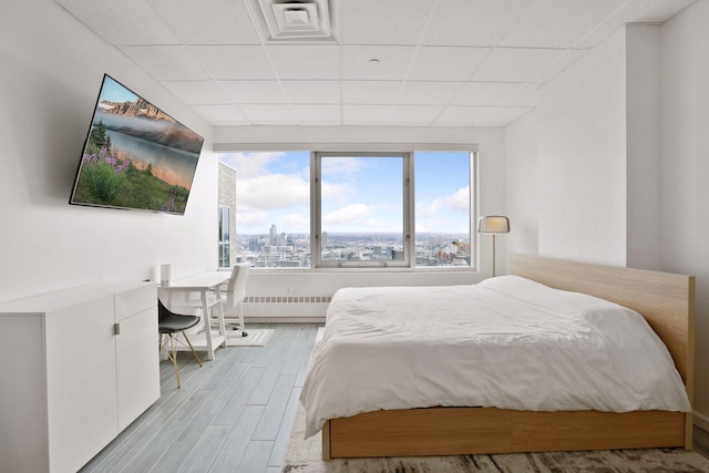 bedroom with radiator, a drop ceiling, and light hardwood / wood-style floors