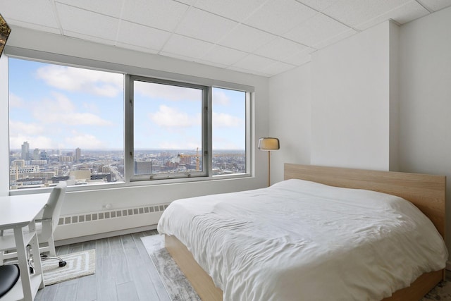 bedroom featuring a paneled ceiling, radiator heating unit, and hardwood / wood-style floors