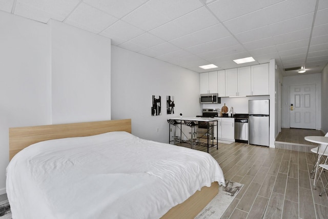 bedroom with a paneled ceiling and stainless steel fridge