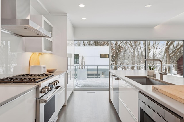 kitchen featuring sink, white cabinetry, high end stove, and wall chimney exhaust hood