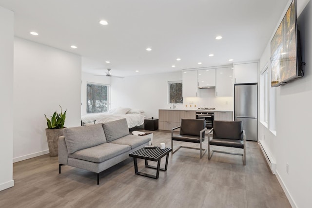 living room with a baseboard radiator, ceiling fan, and light hardwood / wood-style floors