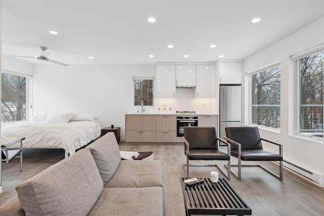 bedroom featuring stainless steel refrigerator, light wood-type flooring, ceiling fan, a baseboard heating unit, and sink