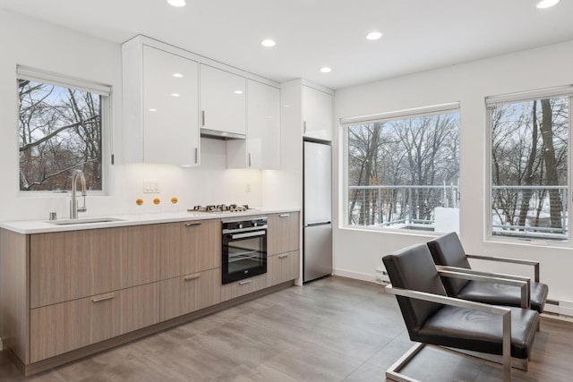 kitchen featuring white gas stovetop, stainless steel refrigerator, black oven, sink, and white cabinetry