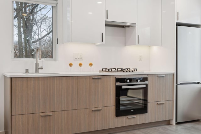 kitchen featuring refrigerator, gas cooktop, oven, white cabinetry, and sink