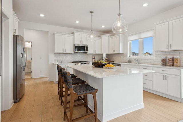 kitchen featuring appliances with stainless steel finishes, light wood-type flooring, a kitchen island, white cabinetry, and hanging light fixtures