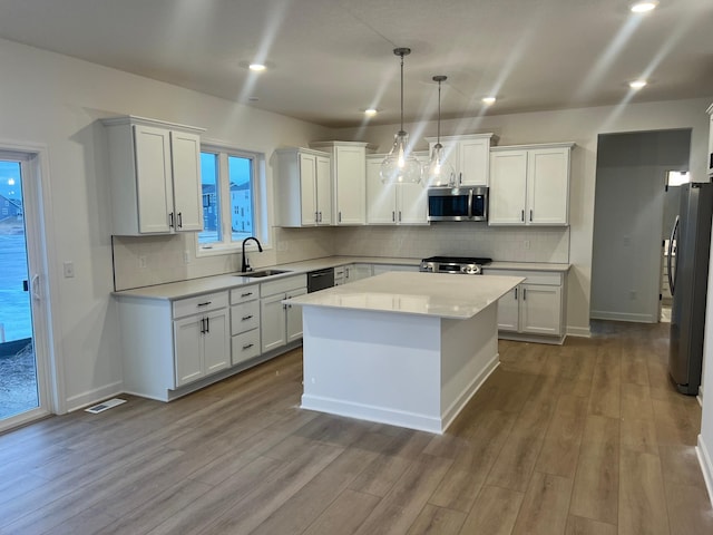 kitchen featuring stainless steel appliances, a kitchen island, hanging light fixtures, and white cabinets