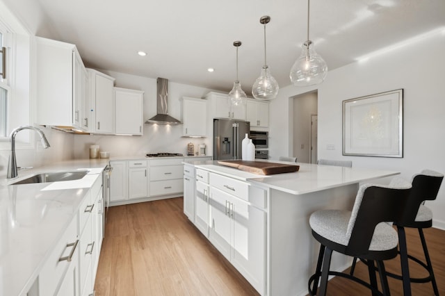 kitchen with white cabinets, stainless steel appliances, a kitchen island, and wall chimney range hood