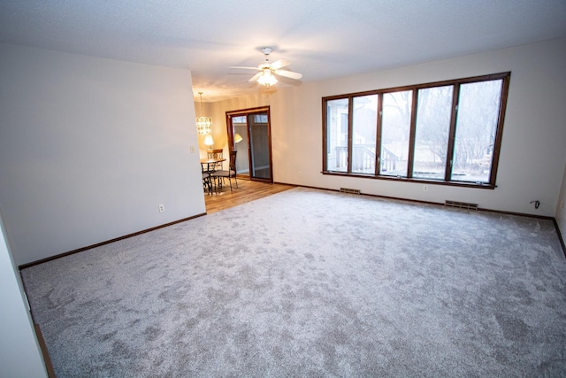 carpeted spare room featuring ceiling fan with notable chandelier