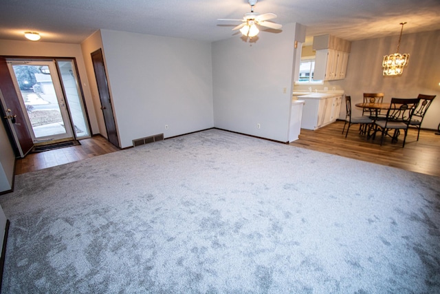 unfurnished living room featuring carpet, ceiling fan with notable chandelier, and a wealth of natural light