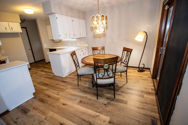 dining space with light wood-type flooring, sink, and an inviting chandelier