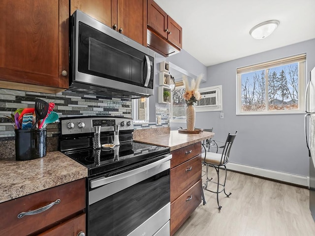 kitchen with backsplash, stainless steel appliances, light stone counters, an AC wall unit, and light wood-type flooring