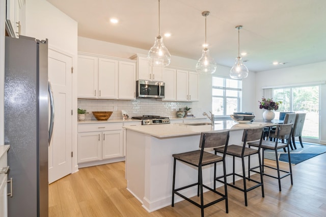 kitchen featuring appliances with stainless steel finishes, decorative light fixtures, sink, white cabinetry, and a center island with sink