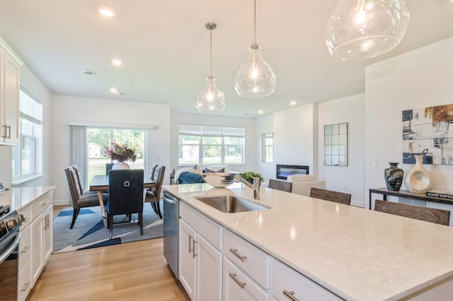 kitchen with a kitchen island with sink, stainless steel dishwasher, sink, white cabinets, and pendant lighting