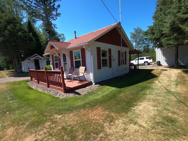 rear view of house with a lawn, a wooden deck, and an outbuilding