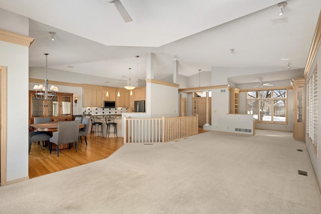 living area featuring light carpet, visible vents, vaulted ceiling, and ceiling fan with notable chandelier