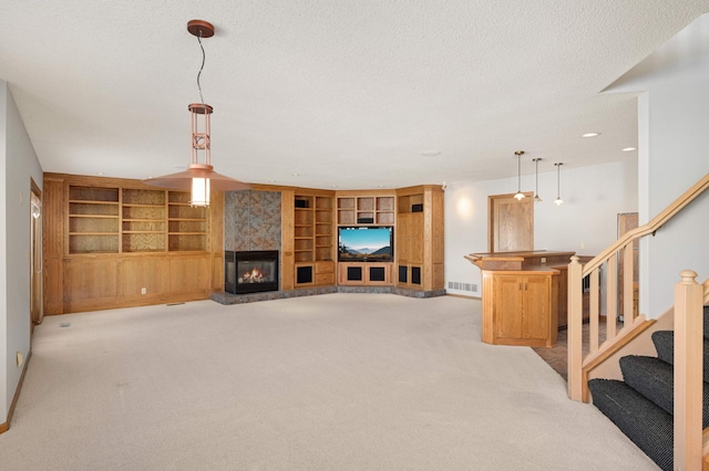 living area with a textured ceiling, built in shelves, light colored carpet, a fireplace, and stairway