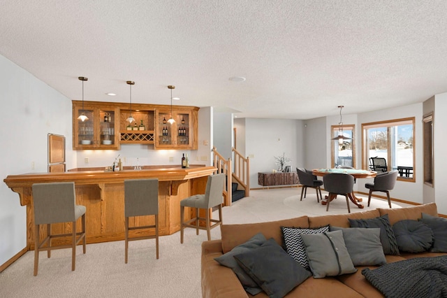 interior space with a textured ceiling, light colored carpet, baseboards, hanging light fixtures, and indoor wet bar