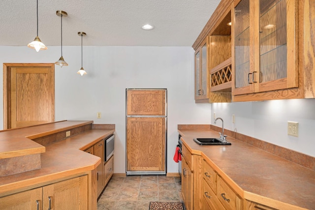 kitchen with hanging light fixtures, a textured ceiling, a sink, and built in appliances