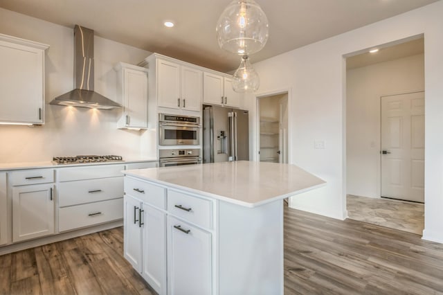 kitchen featuring appliances with stainless steel finishes, wall chimney exhaust hood, pendant lighting, a center island, and white cabinetry