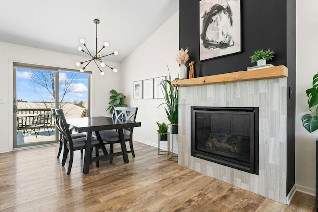 dining area with vaulted ceiling, wood finished floors, a chandelier, a tile fireplace, and baseboards