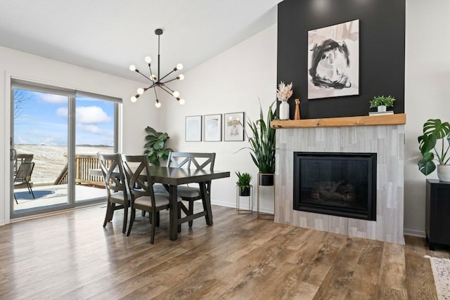 dining room with vaulted ceiling, wood finished floors, a chandelier, a tile fireplace, and baseboards