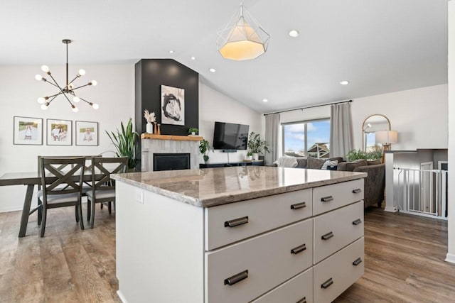 kitchen featuring vaulted ceiling, a fireplace, white cabinets, and wood finished floors