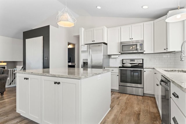 kitchen featuring lofted ceiling, wood finished floors, a sink, appliances with stainless steel finishes, and a center island