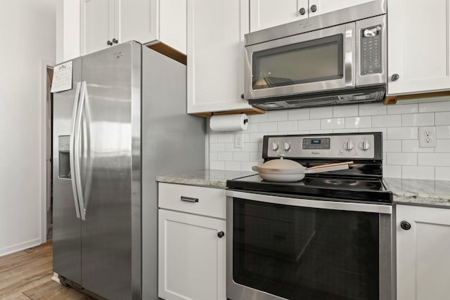 kitchen featuring light stone counters, stainless steel appliances, light wood-style floors, white cabinets, and tasteful backsplash