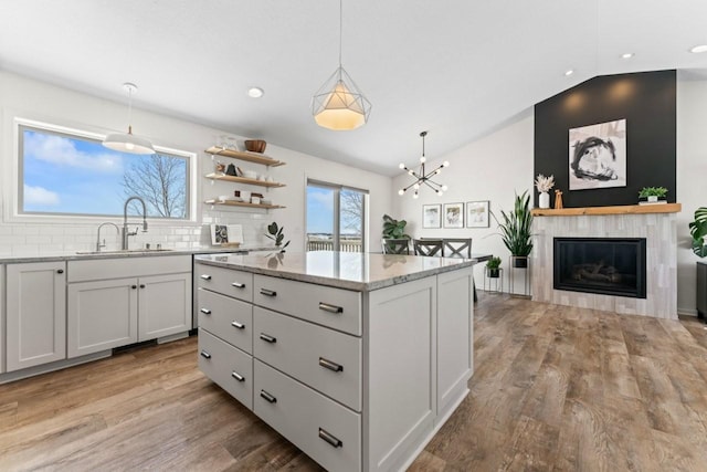 kitchen featuring a kitchen island, a sink, light wood-style floors, light stone countertops, and decorative light fixtures