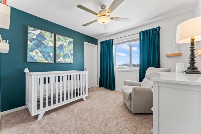 bedroom with a crib, carpet, baseboards, and a ceiling fan