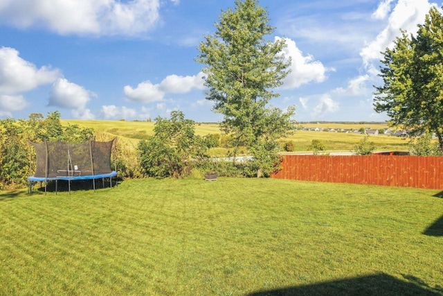 view of yard featuring a trampoline, fence, and a rural view