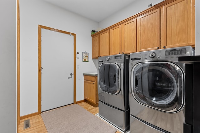 laundry room featuring separate washer and dryer, light hardwood / wood-style floors, and cabinets