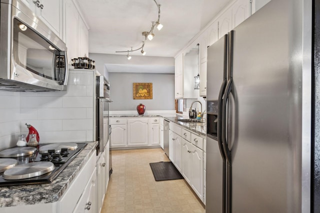 kitchen with tasteful backsplash, dark stone countertops, stainless steel appliances, white cabinets, and sink