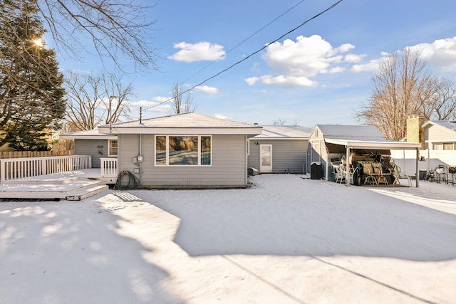 snow covered back of property with a wooden deck and a carport