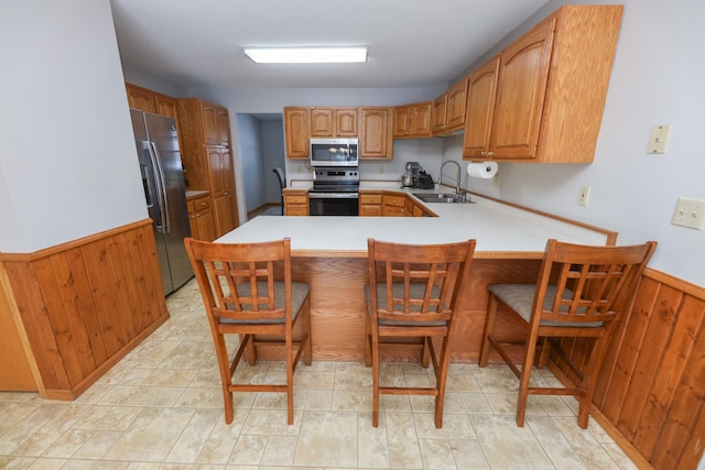 kitchen with appliances with stainless steel finishes, wooden walls, sink, a breakfast bar area, and kitchen peninsula