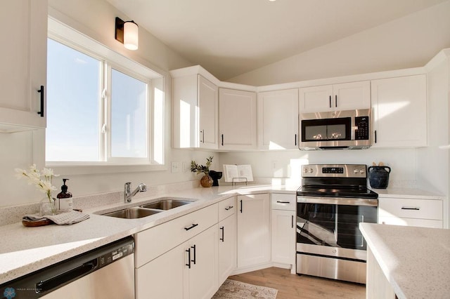 kitchen featuring light stone countertops, sink, vaulted ceiling, white cabinets, and appliances with stainless steel finishes