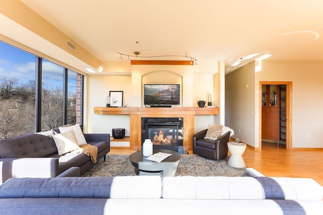 living area featuring baseboards, visible vents, a glass covered fireplace, wood finished floors, and track lighting