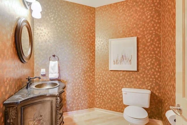 bathroom featuring wood finished floors, vanity, toilet, and wallpapered walls