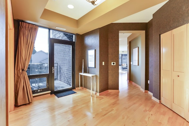 foyer entrance featuring baseboards, a tray ceiling, visible vents, and light wood-style floors