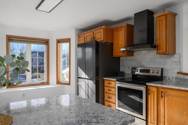 kitchen featuring backsplash, black fridge, light stone countertops, wall chimney range hood, and electric stove