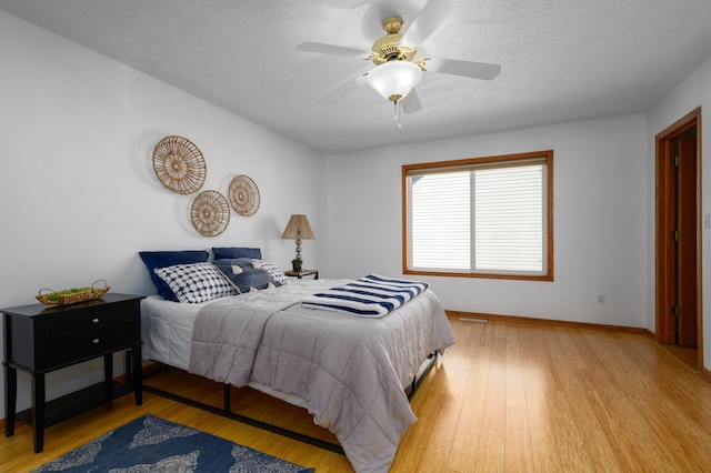 bedroom with a textured ceiling, ceiling fan, and light wood-type flooring