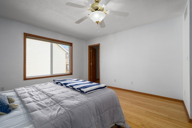 bedroom with a textured ceiling, ceiling fan, and light wood-type flooring