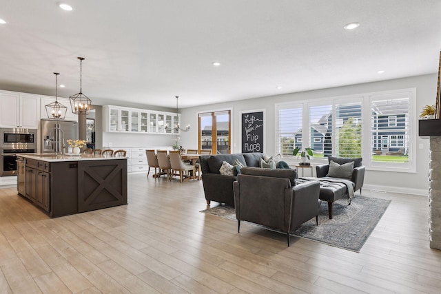 living area featuring a notable chandelier, light wood finished floors, baseboards, and recessed lighting