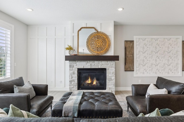 living room featuring recessed lighting, a stone fireplace, baseboards, and wood finished floors