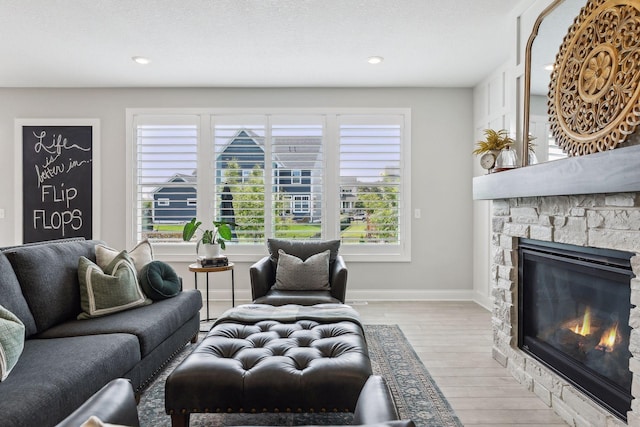 living room with recessed lighting, a stone fireplace, baseboards, and wood finished floors