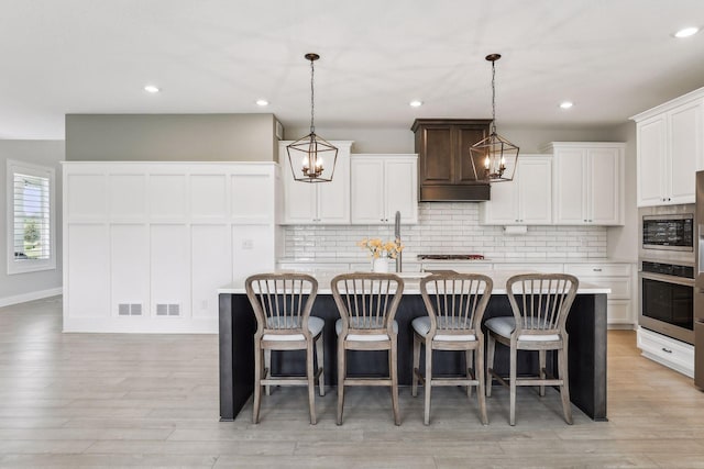 kitchen featuring light wood finished floors, stainless steel appliances, light countertops, backsplash, and an island with sink