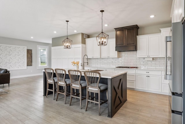 kitchen featuring a breakfast bar, tasteful backsplash, light wood-style floors, freestanding refrigerator, and an island with sink